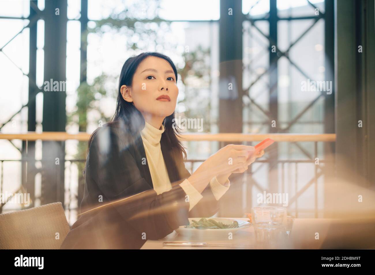 Selbstbewusste Geschäftsfrau mit Mobiltelefon in der Cafeteria im Büro Stockfoto