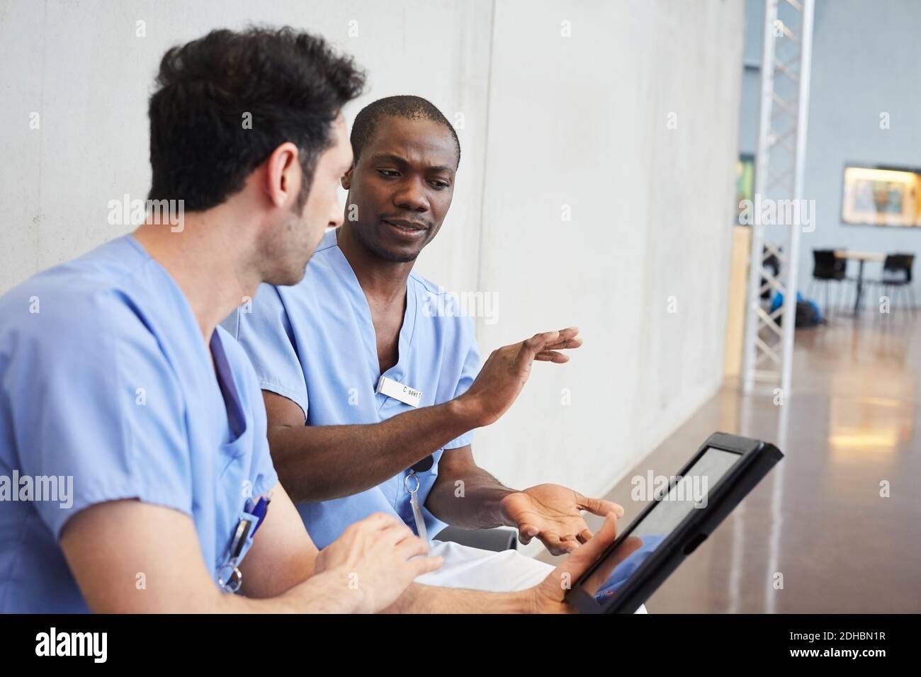 Männliche Krankenschwestern diskutieren über digitale Tablette, während im Flur sitzen Im Krankenhaus Stockfoto