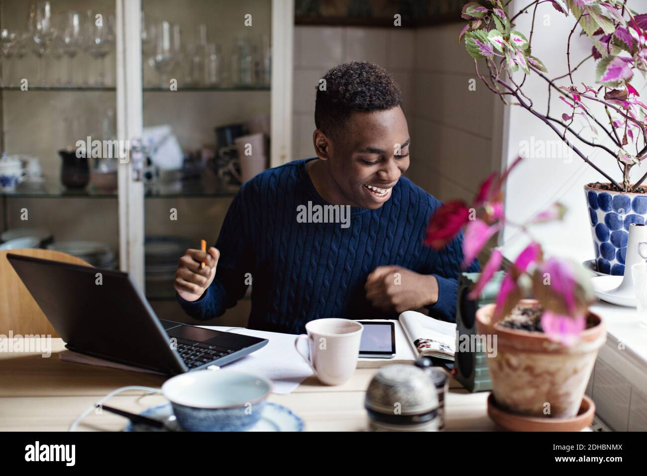 Fröhlicher Teenager-Junge, der Buch liest, während er zu Hause studiert Stockfoto