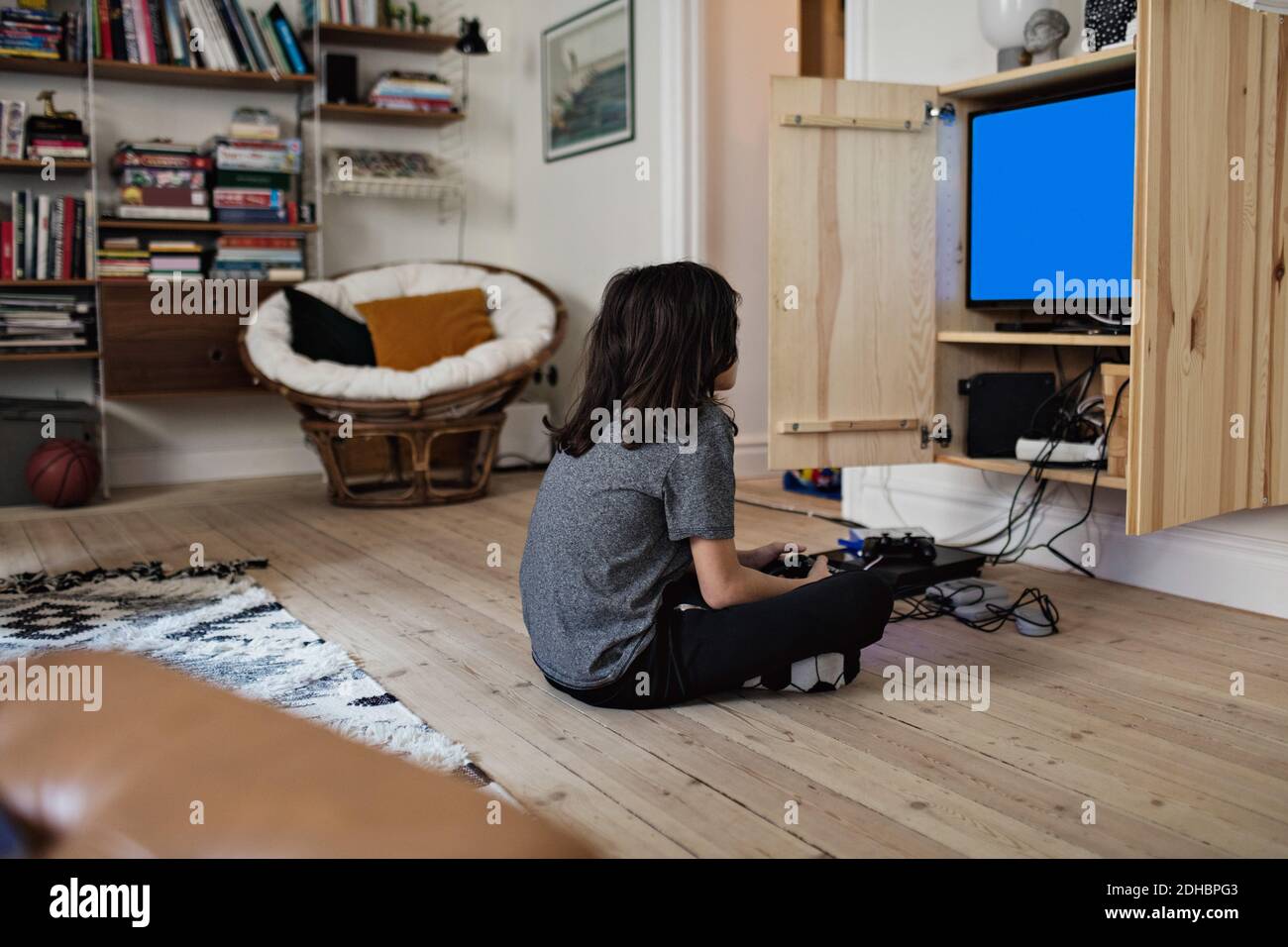 Seitenansicht des Jungen, der Videospiel spielt, während er auf sitzt hartholzboden zu Hause Stockfoto