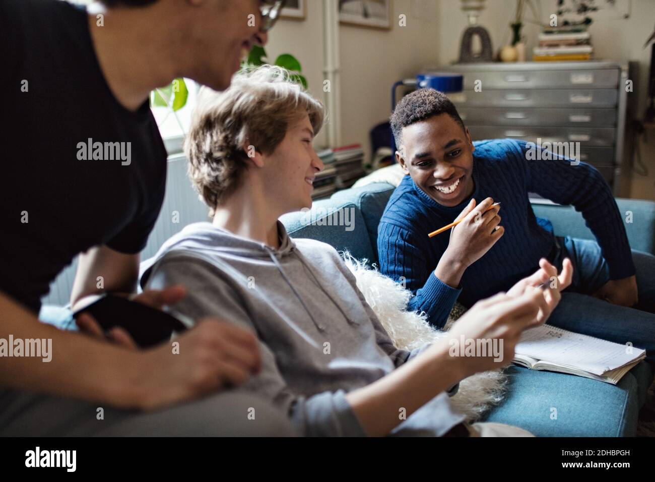 Lächelnder Teenager, der Freunden auf dem Sofa das Handy zeigt Während des Studiums zu Hause Stockfoto