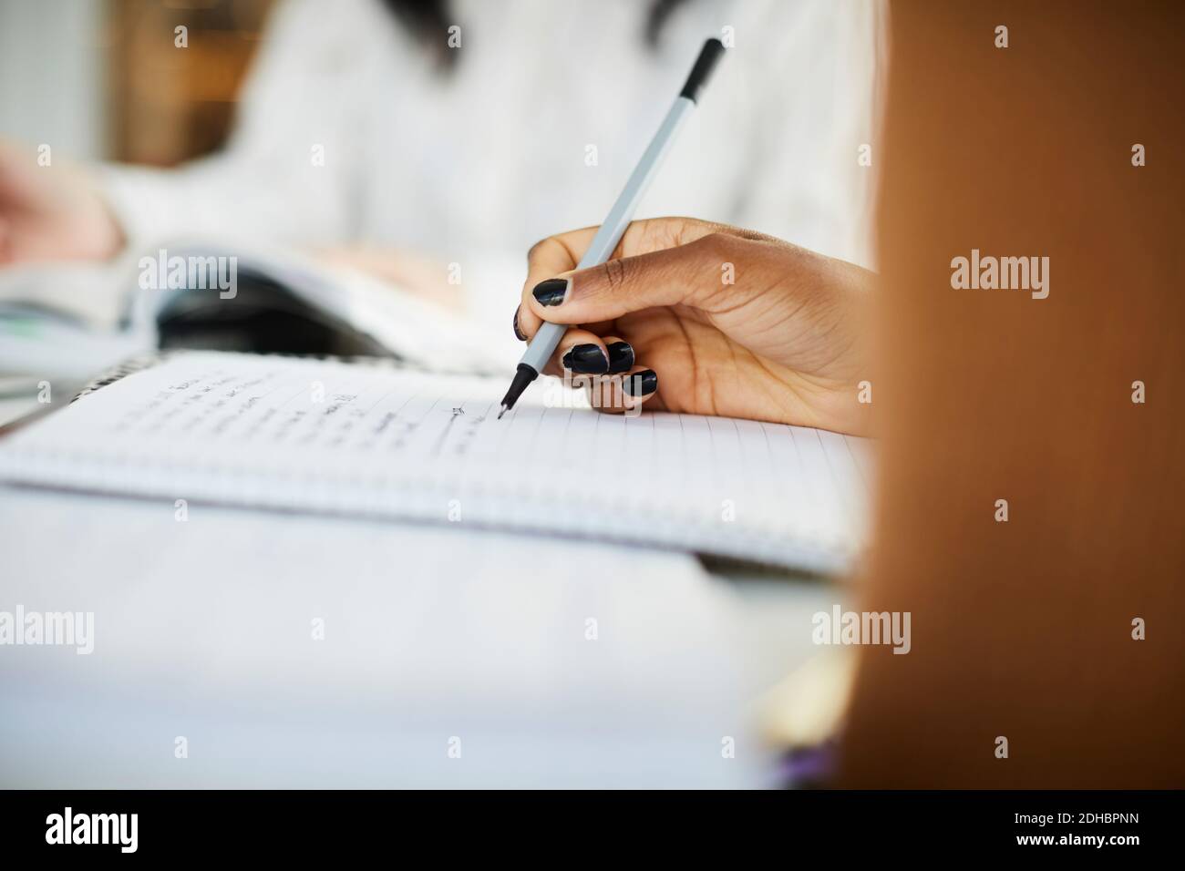 Kurze Hand der Frau, die auf Buch schreibt, während sie studiert Tabelle Stockfoto