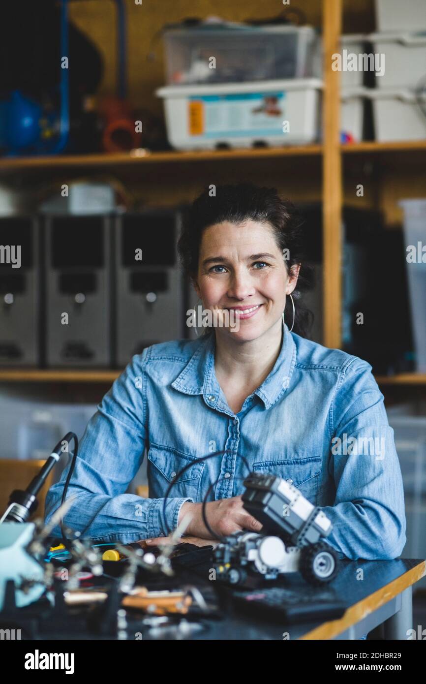 Portrait von selbstbewussten reifen Lehrerin sitzen mit Wissenschaft Projekt Am Schreibtisch im Klassenzimmer in der High School Stockfoto