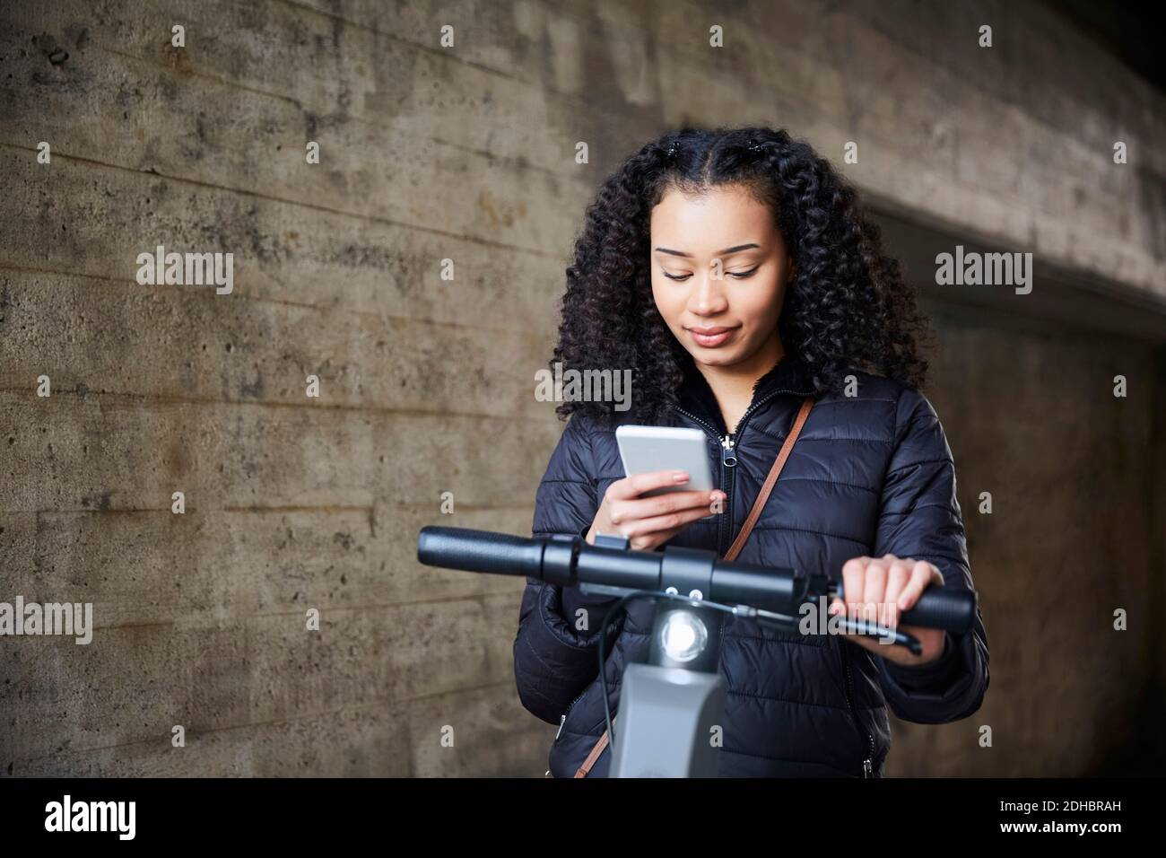 Teenager-Mädchen mit elektrischen Push-Roller mit Handy durch Wand Stockfoto