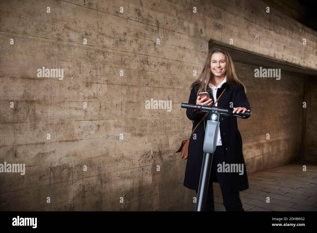 Portrait von lächelnd Teenager-Mädchen mit Elektro-Push-Roller durch Wand Stockfoto