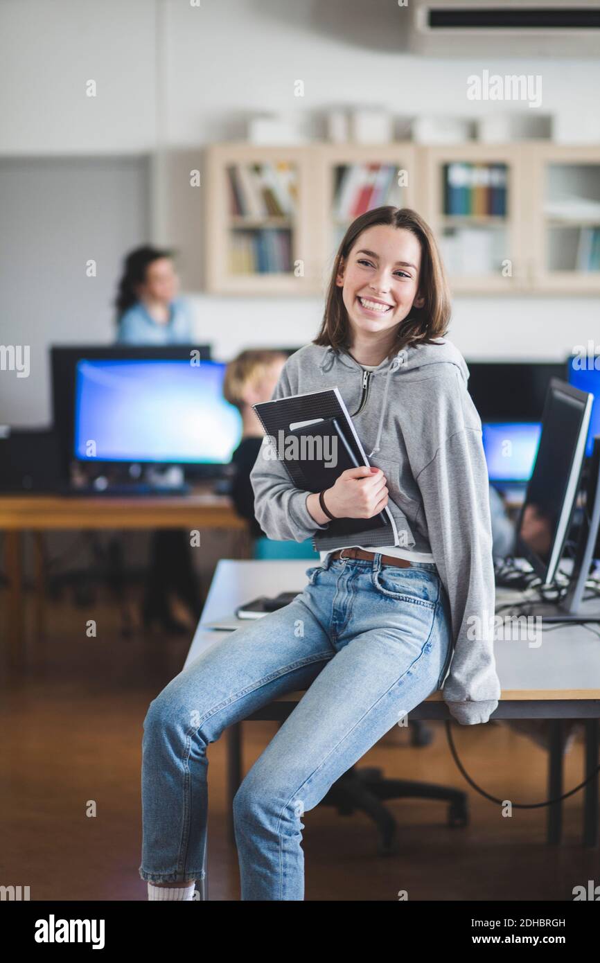 Fröhliche Schülerin der High School, die mit Büchern auf dem Schreibtisch sitzt Im Klassenzimmer Stockfoto