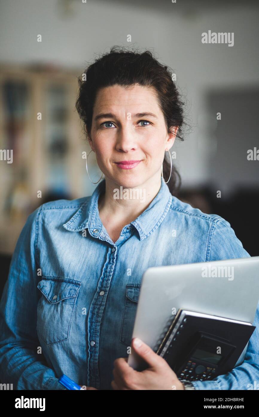 Portrait von selbstbewussten reifen Lehrerin mit Tagebuch und Laptop Im Computerlabor stehen Stockfoto