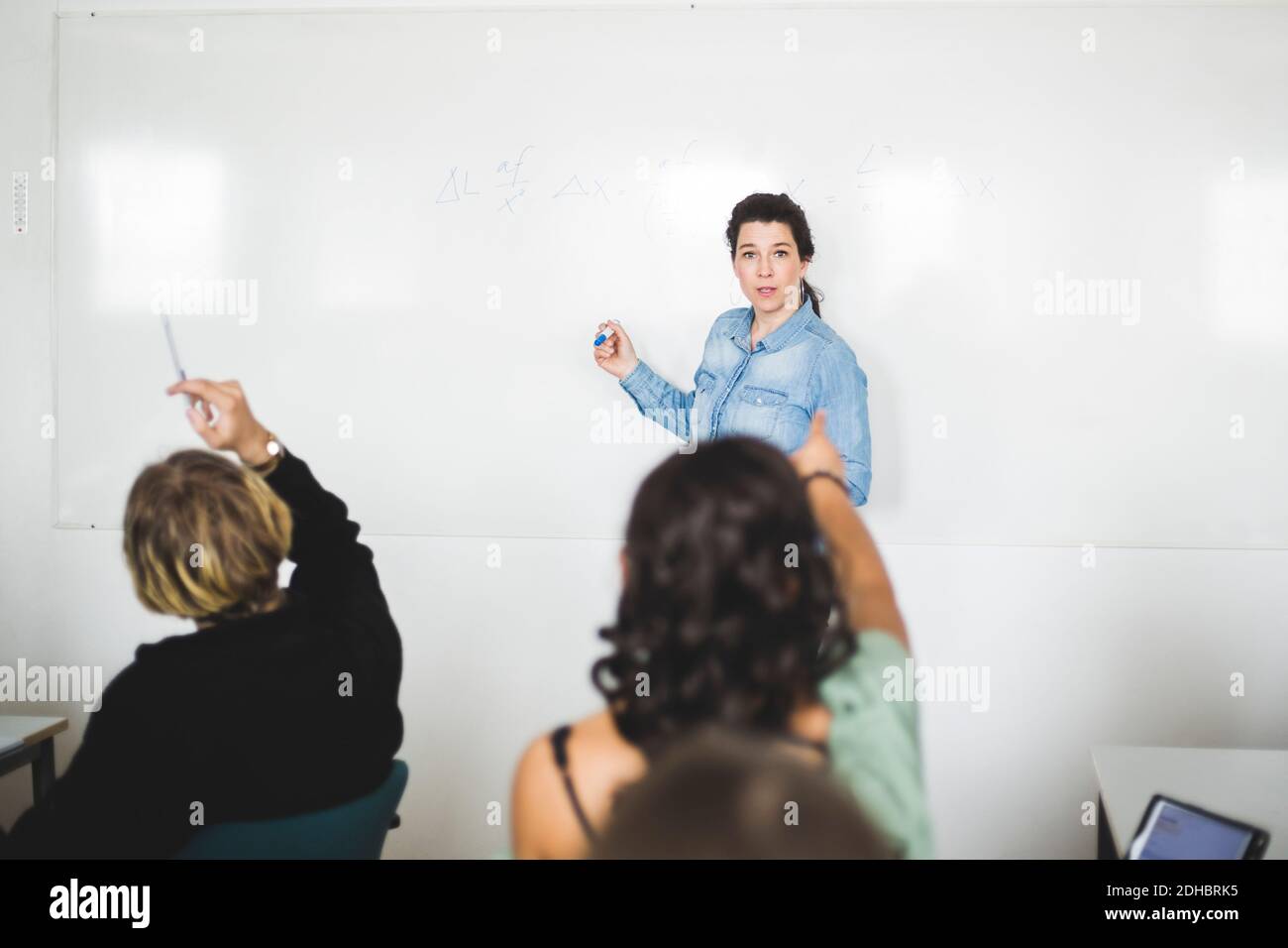 Die Schüler zeigen auf den Lehrer, der im Klassenzimmer gegen das Whiteboard steht Stockfoto