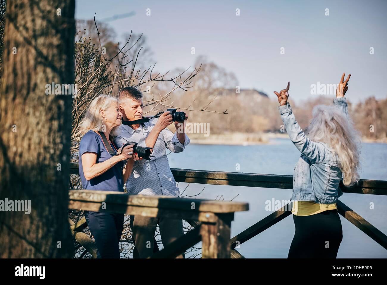 Ältere Männer und Frauen, die einen Freund im Stehen durch die Kamera fotografieren Am See Stockfoto