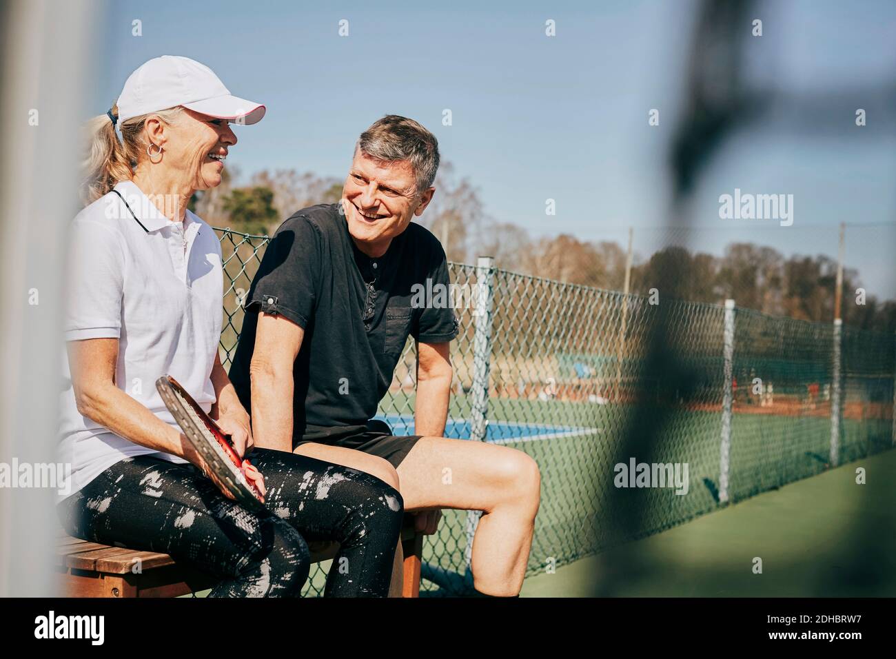 Glücklicher älterer Mann und Frau sprechen, während auf der Bank sitzen Auf dem Tennisplatz Stockfoto