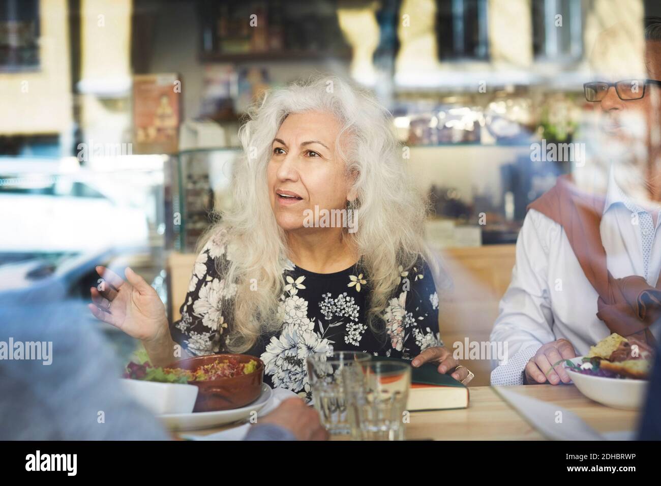 Ältere Frau im Buchclub im Restaurant im Gespräch mit Freunden Durch Glasfenster gesehen Stockfoto