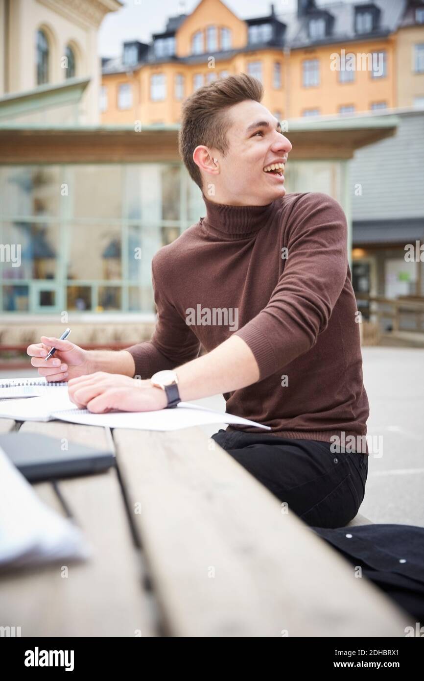 Lächelnder Teenager, der über die Schulter schaut, während er am Tisch sitzt Auf dem Schulhof Stockfoto