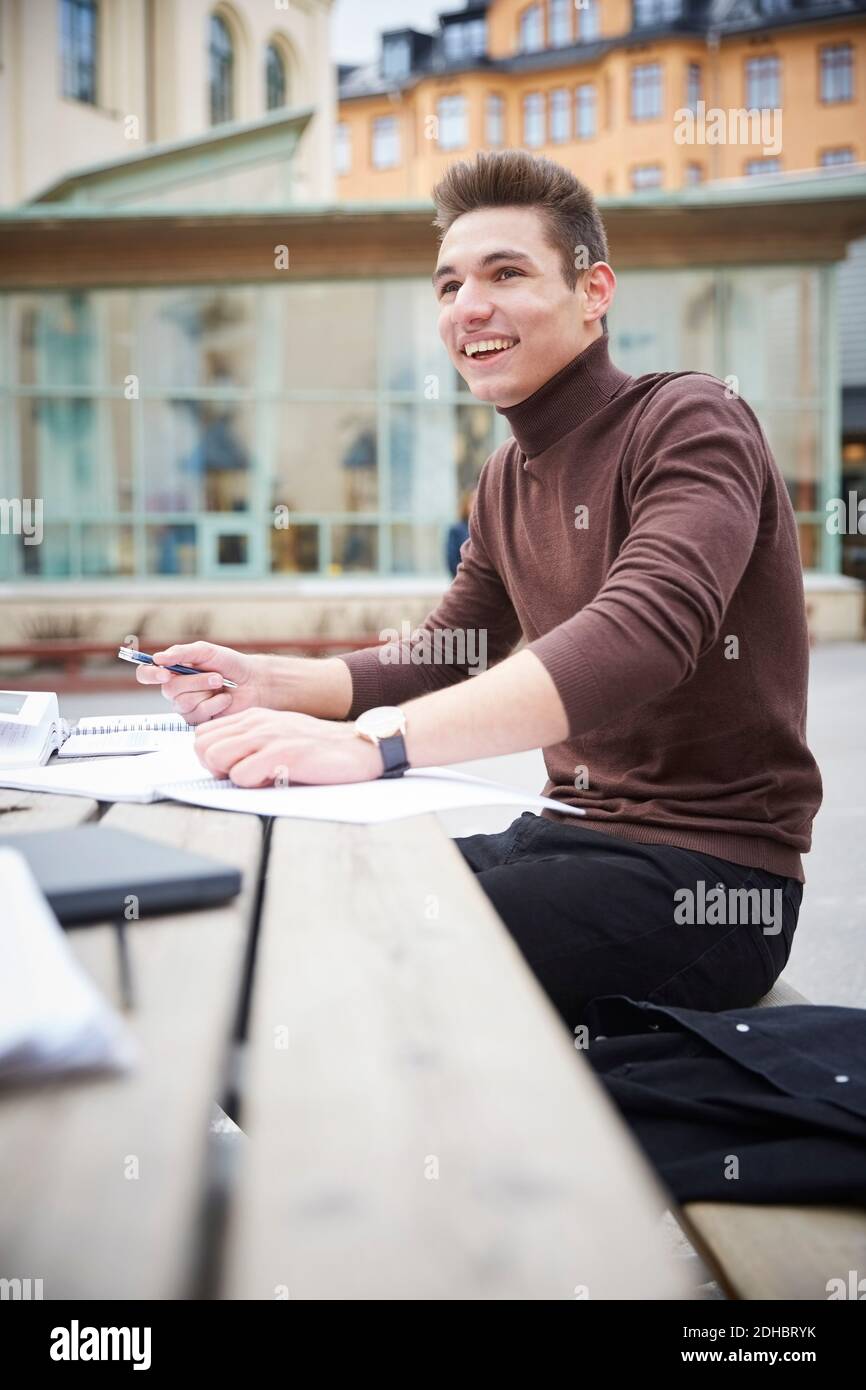 Lächelnder Teenager schaut weg, während er an einem Tisch sitzt Schulhof Stockfoto