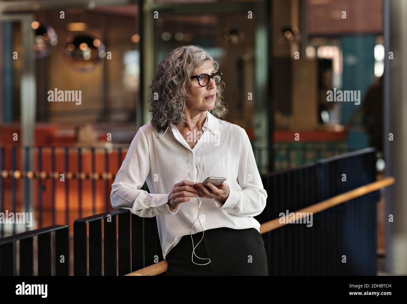 Erwägen, eine Geschäftsfrau mit einem Smartphone zu benutzen, während sie am Geländer steht Im Büro Stockfoto