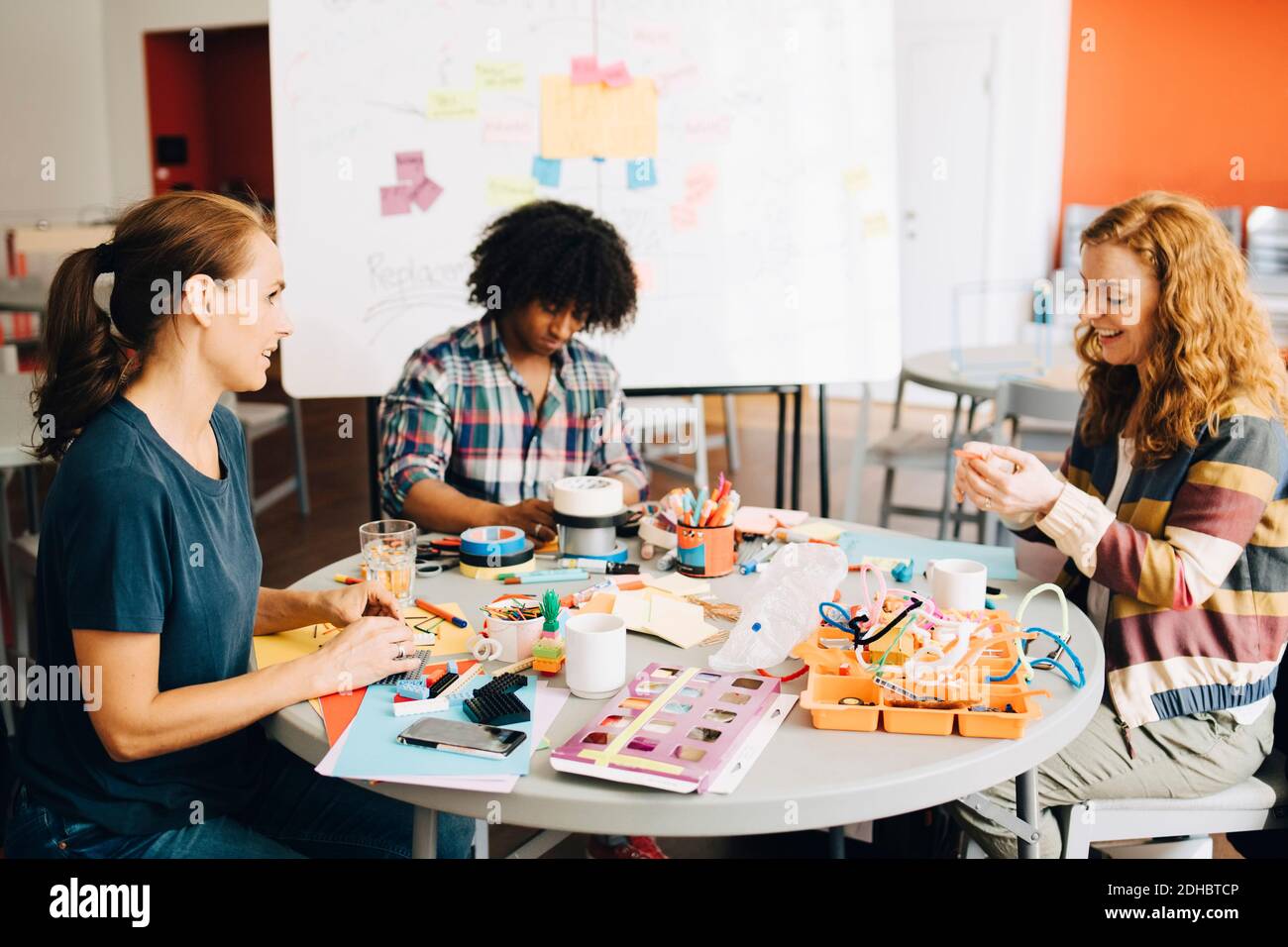 Lächelnd Mitte Erwachsene weibliche Ingenieure diskutieren, während Geschäftsmann arbeiten an Tisch im kreativen Büro Stockfoto