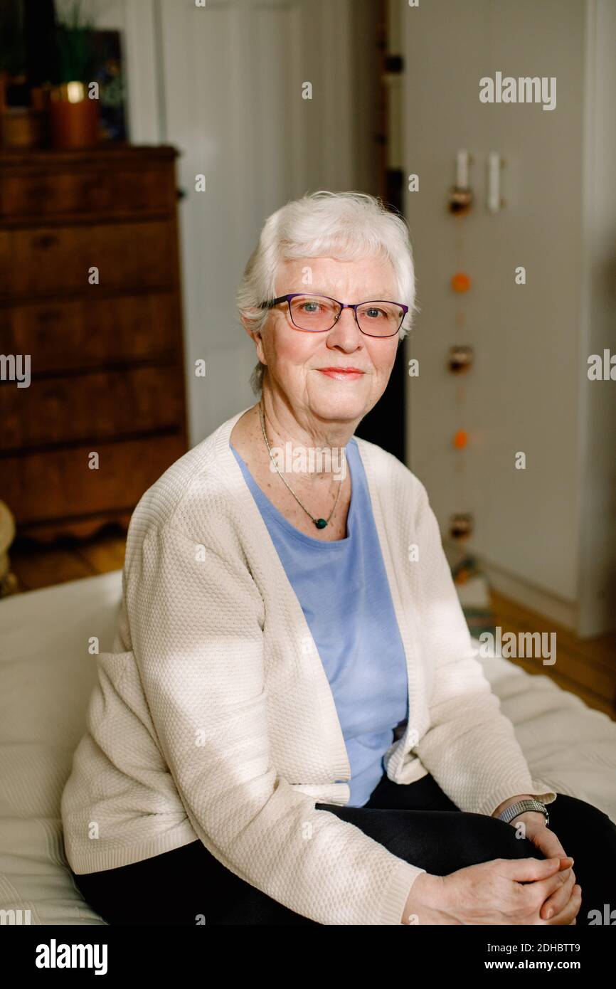 Porträt einer lächelnden Rentnerin im Ruhestand, die auf dem Bett sitzt Pflegeheim Stockfoto