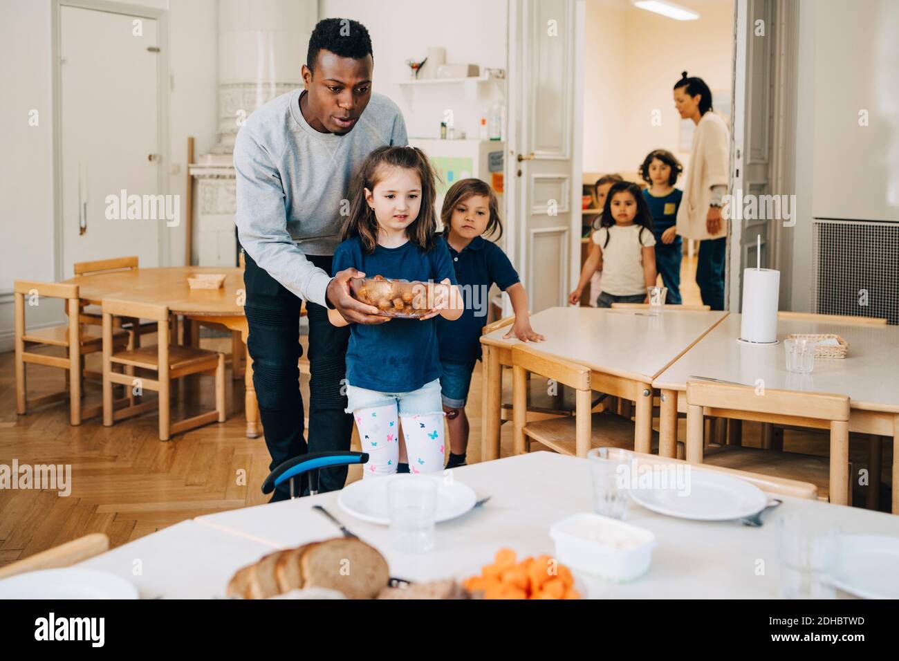 Männlich Lehrer Mädchen beim Tragen von Nahrung Schüssel bei Kind zu unterstützen Präsenzschulung Stockfoto