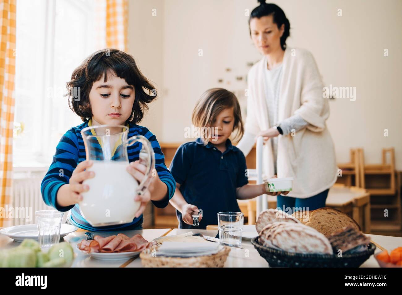 Lehrer, der Jungen bei der Organisation von Essen auf dem Tisch in der Kinderbetreuung behilflich ist Schulungsraum Stockfoto