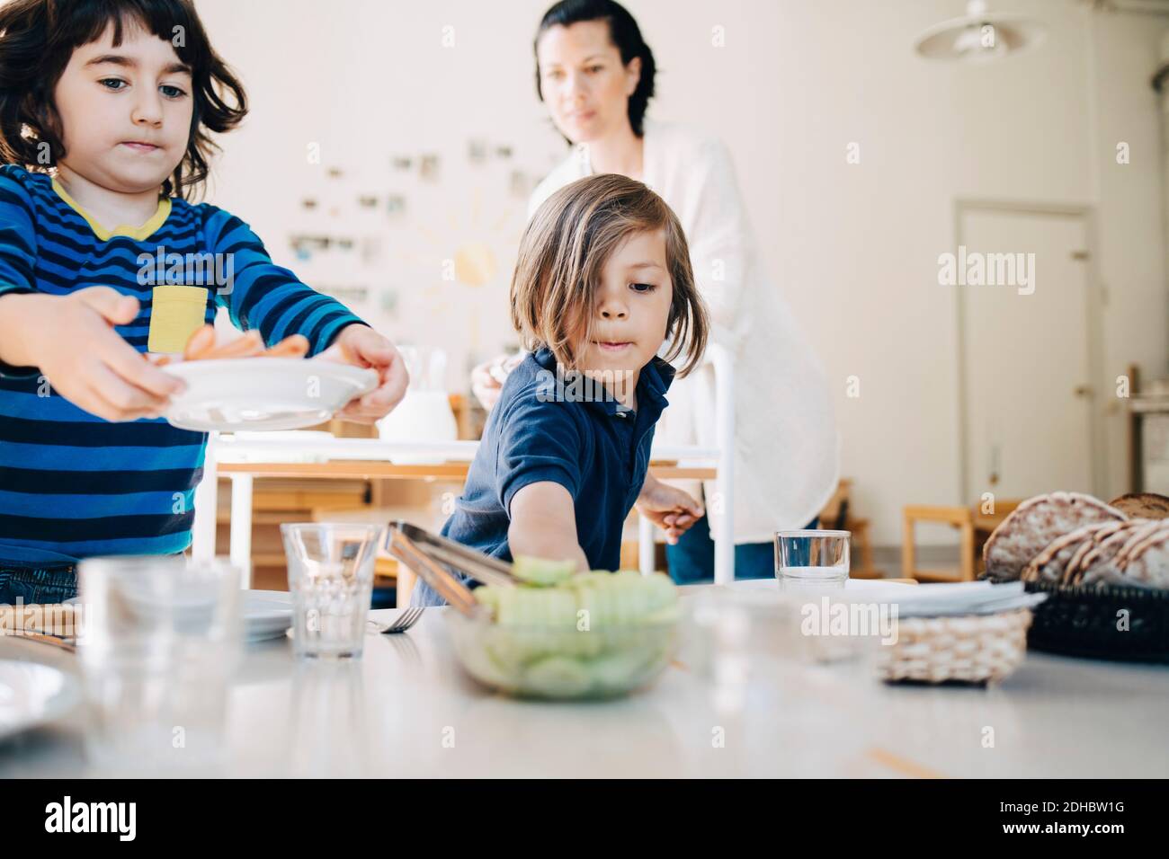 Lehrer, der Jungen dabei hilft, Essen auf dem Tisch im Klassenzimmer zu arrangieren Kinderbetreuung Stockfoto