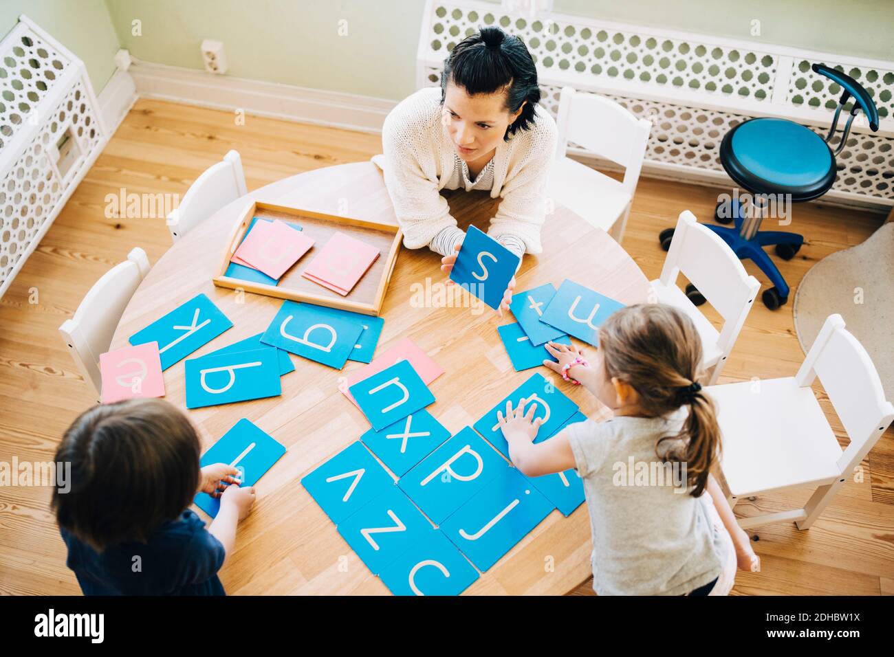 High-Winkel-Ansicht der zuversichtlich weibliche Lehrer zeigt Buchstaben S An Schüler am Tisch im Klassenzimmer Stockfoto