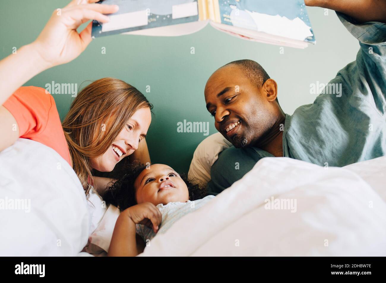 Glückliche Eltern zeigen Storybook zu Tochter während schlafen zusammen auf Bett zu Hause Stockfoto
