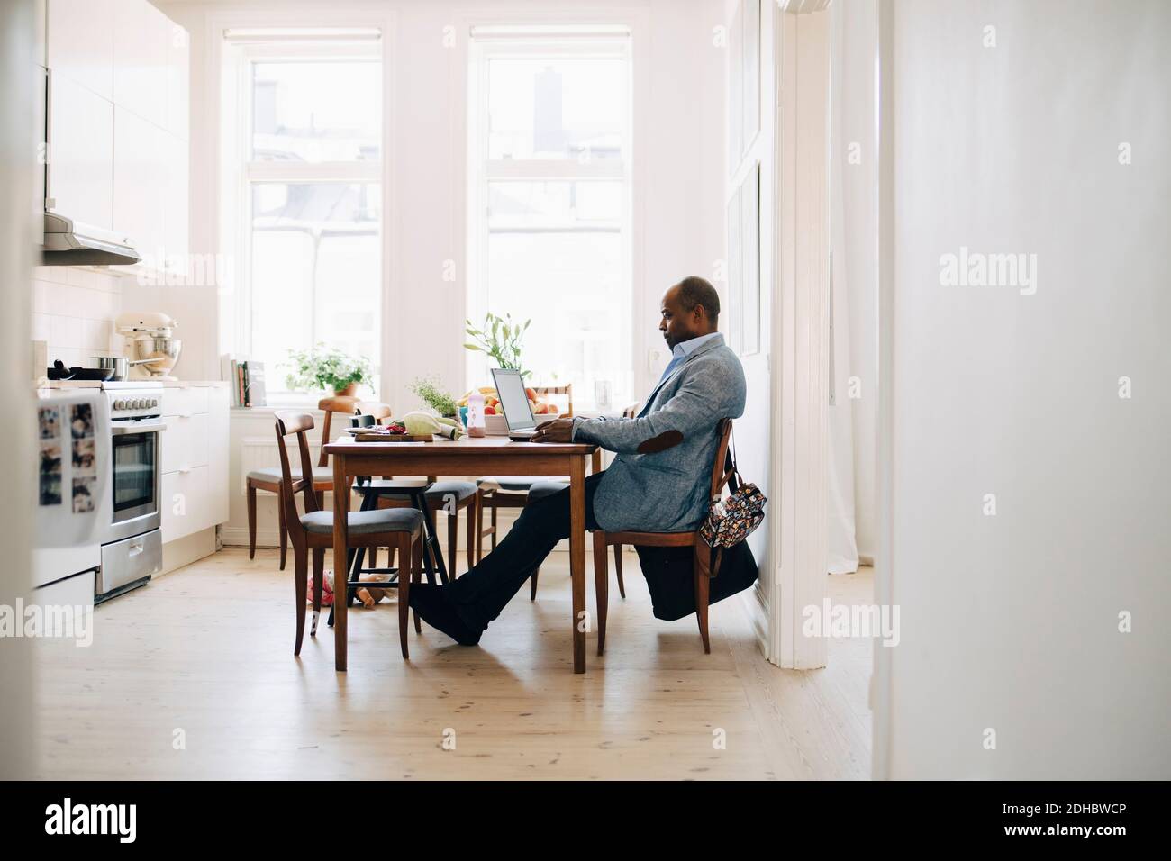 Volle Länge der reifen Mann arbeiten auf Laptop, während sitzen In der Küche zu Hause Stockfoto