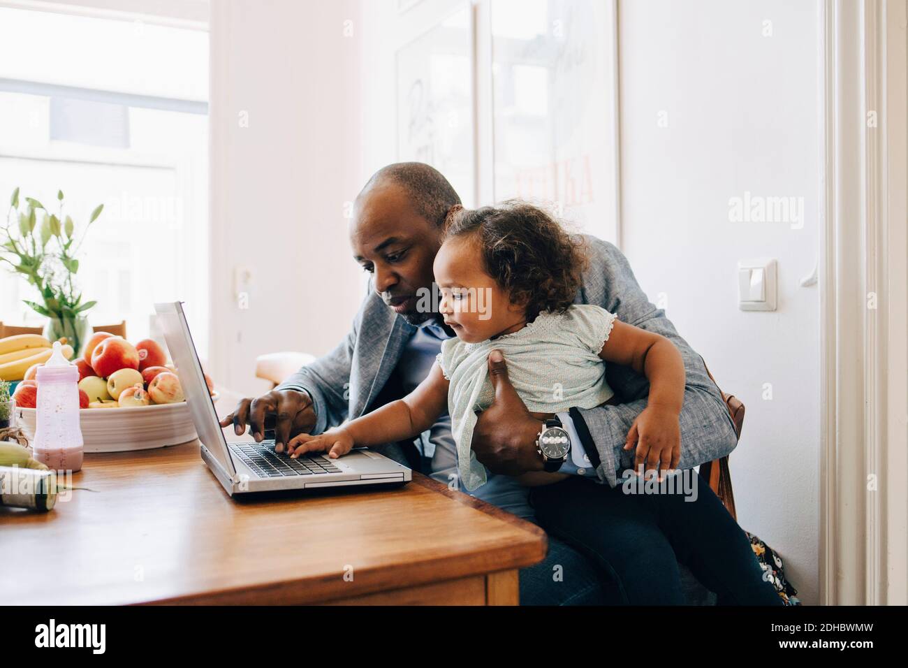 Vater zeigt der Tochter einen Laptop, während er am Tisch sitzt Esszimmer Stockfoto
