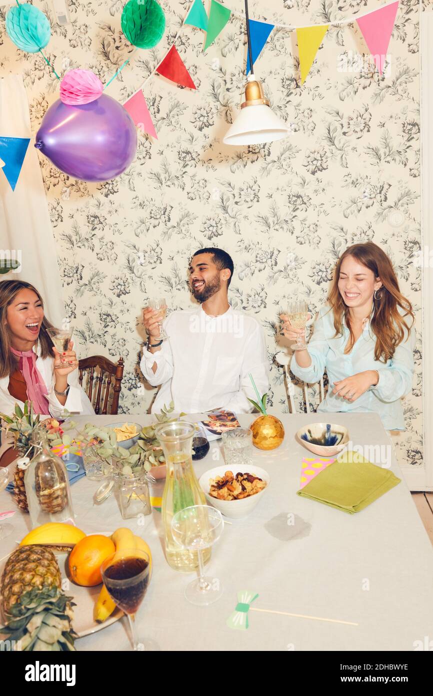 Fröhliche junge Freunde feiern beim Sitzen am Esstisch während Dinnerparty Stockfoto