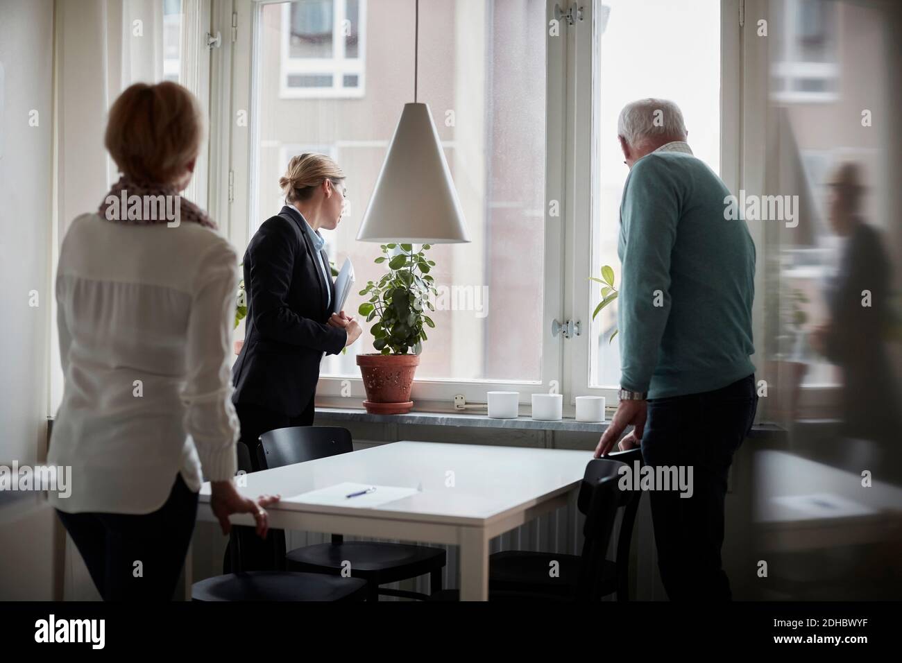 Seniorenpaar und Immobilienmakler, die durch Fenster schauen Neues Zuhause Stockfoto