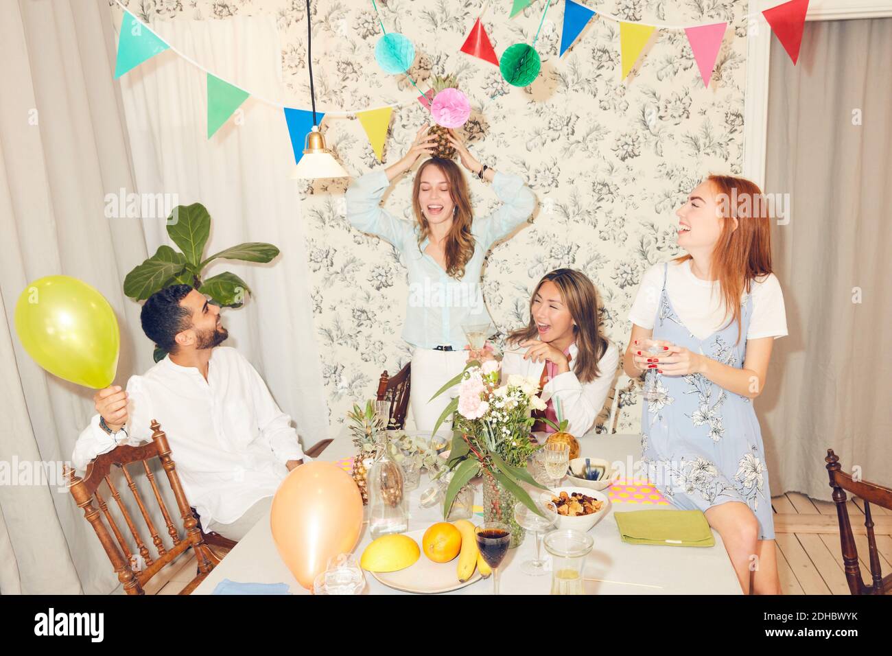 Junge unbeschwerte Freunde spielen mit Ananas beim Abendessen Party an Wohnung Stockfoto