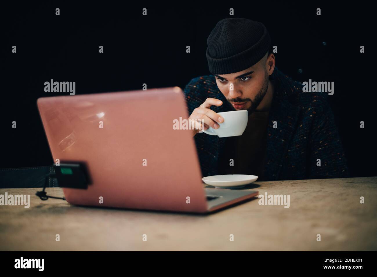 Selbstbewusst junge männliche Hacker trinken Kaffee, während Blick auf Laptop Am Schreibtisch im Büro Stockfoto