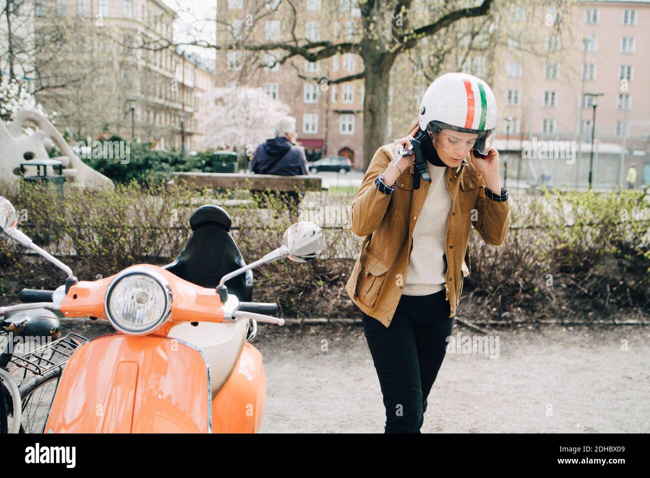 Junge Geschäftsfrau Entfernen Helm beim Gehen mit Motorroller auf Straßenrand in der Stadt Stockfoto
