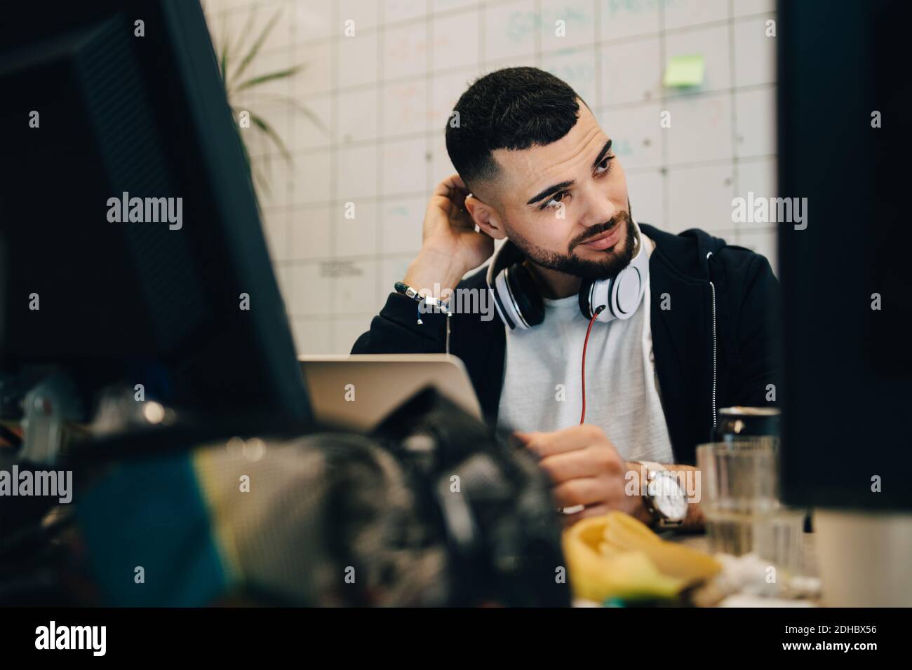 Verwirrt junge männliche Computer-Programmierer kratzen Kopf beim Sitzen mit Laptop im kreativen Büro Stockfoto