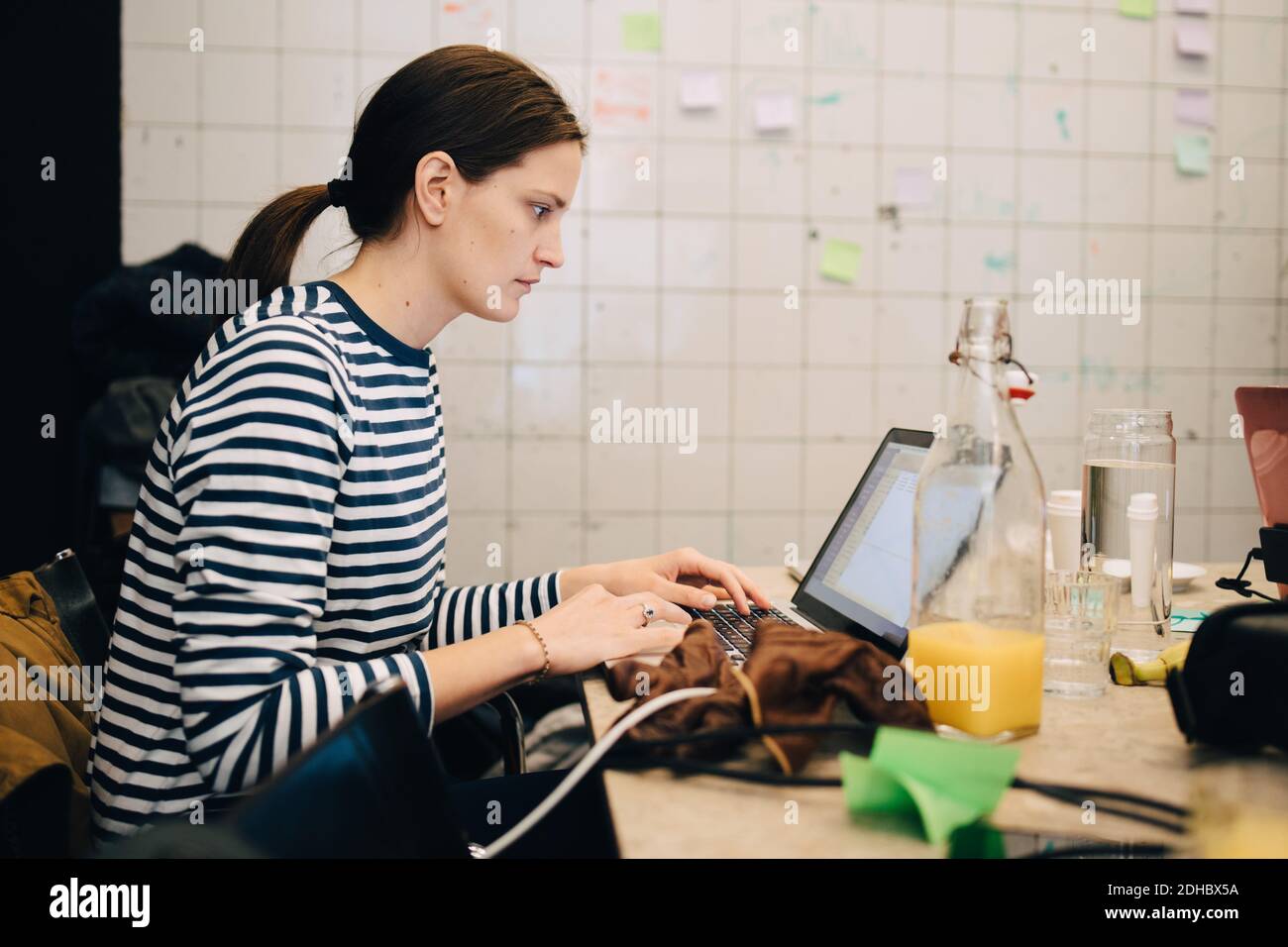 Seitenansicht einer jungen Geschäftsfrau, die im Sitzen auf dem Laptop verschlüsselt Am Schreibtisch in einem kleinen Büro Stockfoto