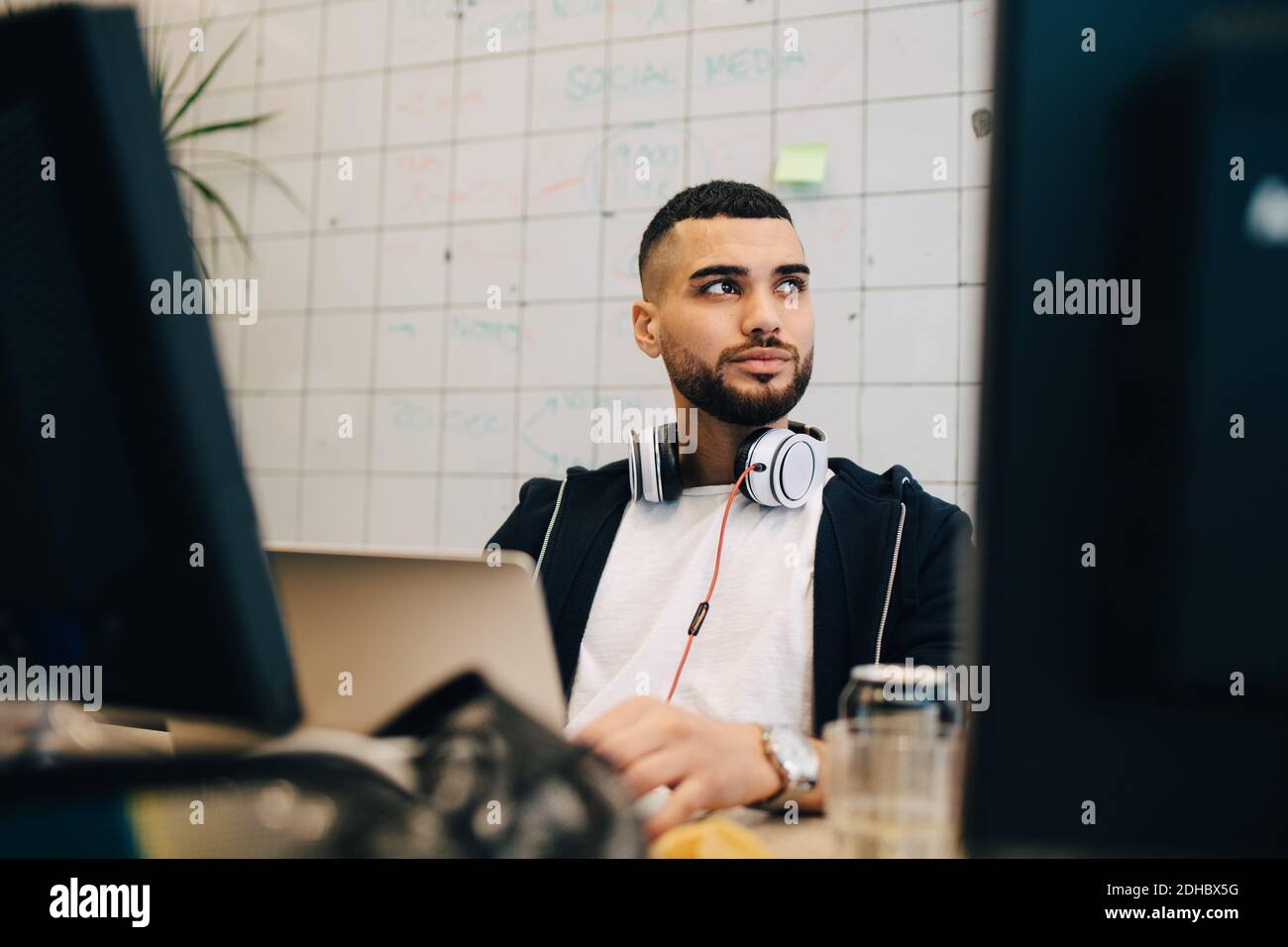 Junger männlicher Computerhacker sitzt mit Laptop und schaut weg Im Kreativbüro Stockfoto