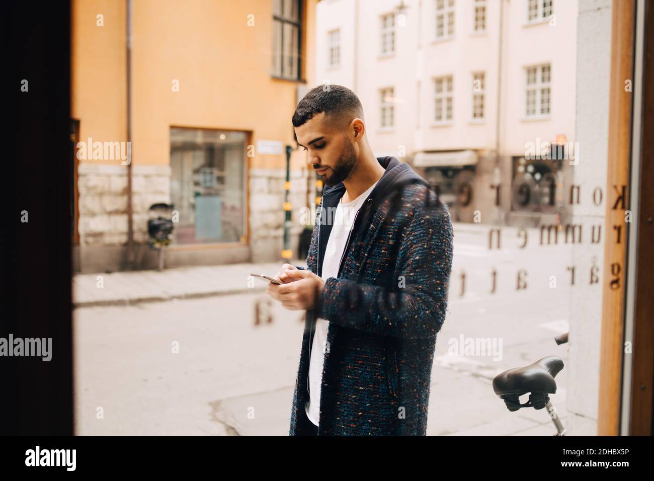 Selbstbewusster junger Geschäftsmann mit Smartphone durch Fenster gesehen Stockfoto