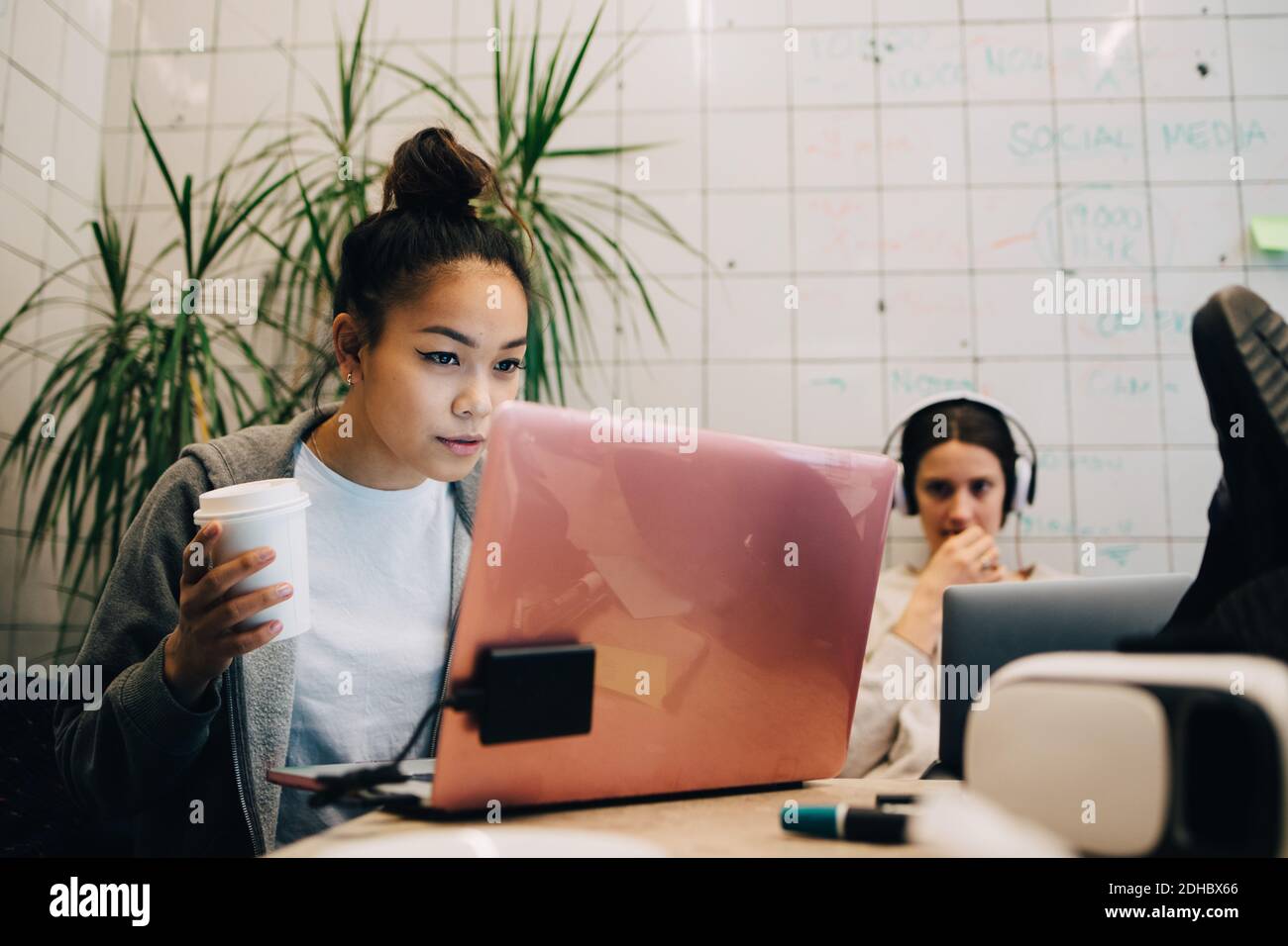 Selbstbewusste junge Geschäftsfrau hält Kaffee, während mit Laptop von weiblich Kollege im Kreativbüro Stockfoto