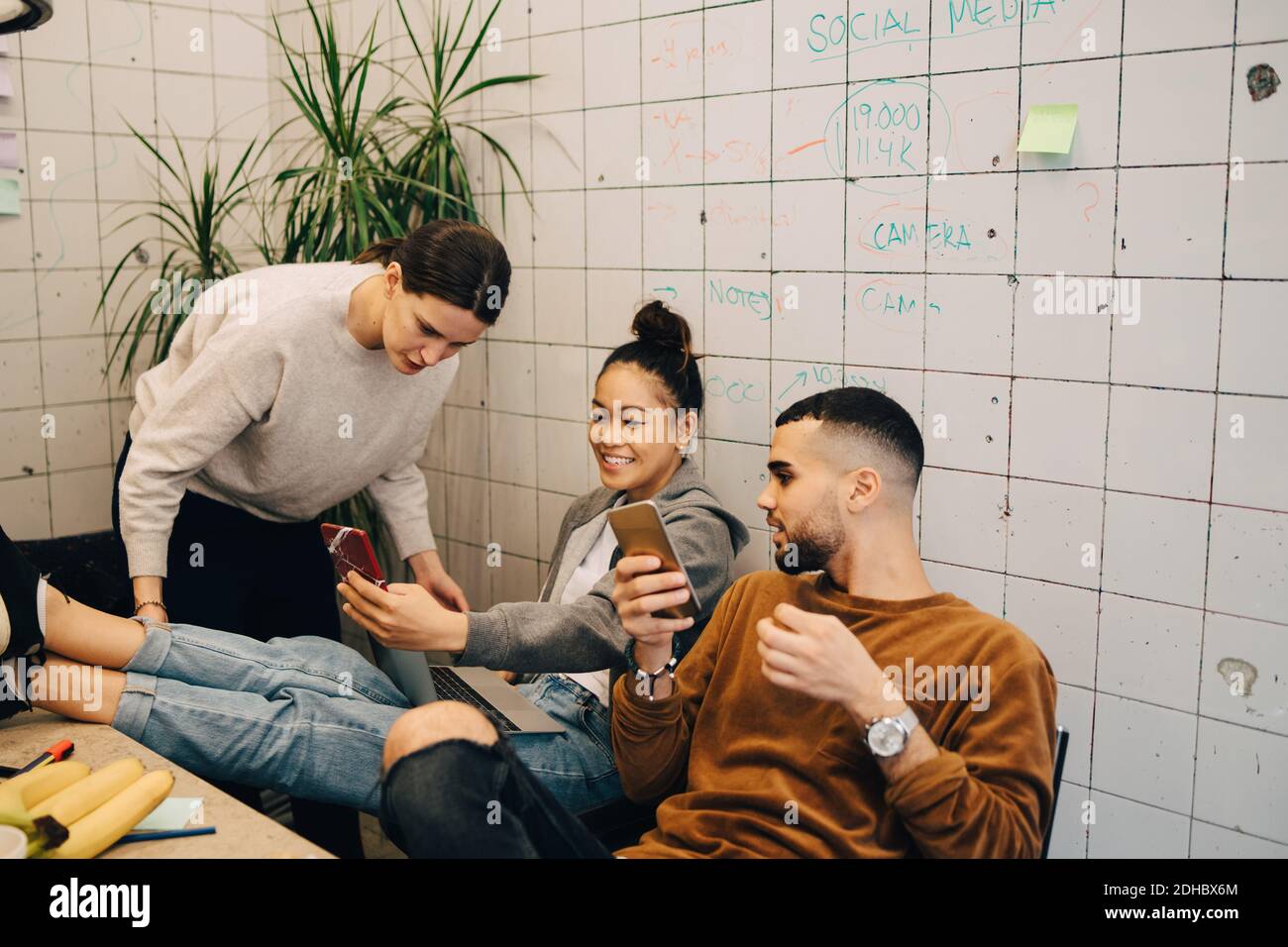 Junge Geschäftsfrau, die Smartphone mit Kollegen teilt, während sie sitzt Kreatives Büro Stockfoto