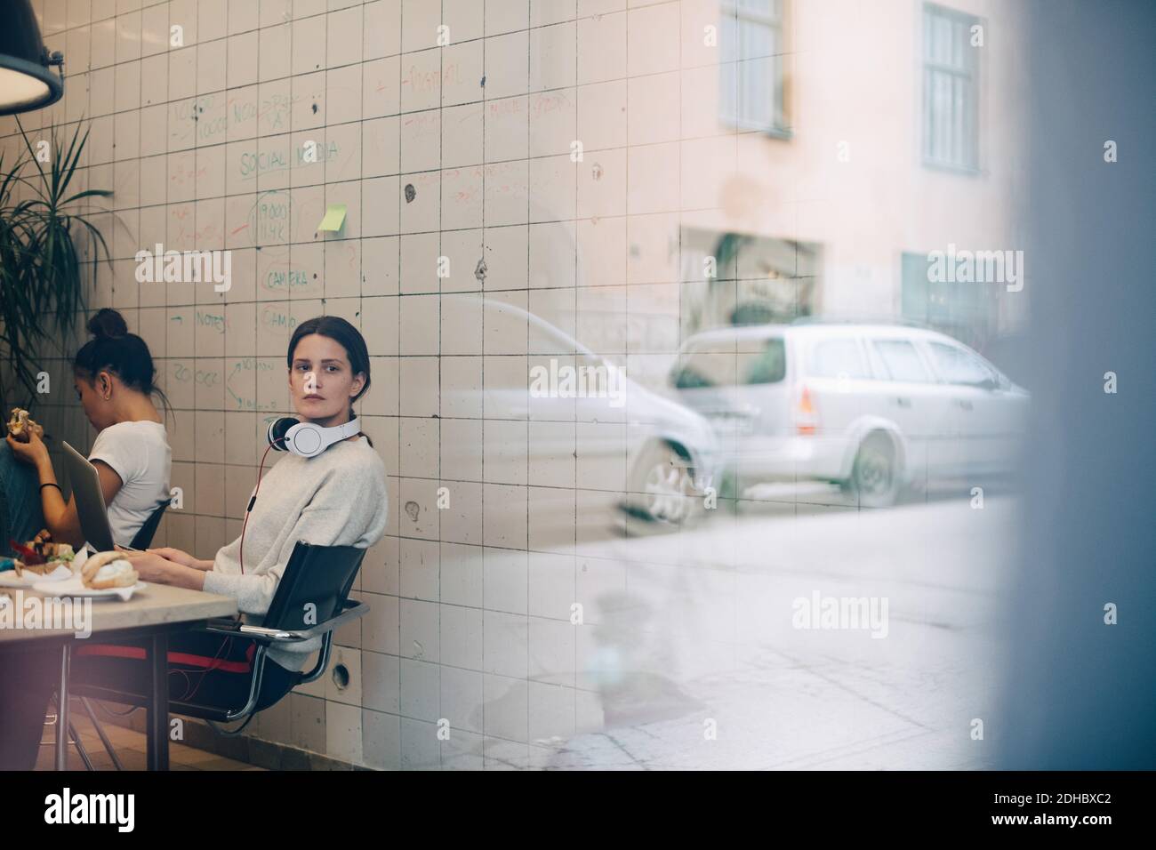 Junge Geschäftsfrau schaut weg, während sie am Schreibtisch in klein sitzt Büro durch Fenster gesehen Stockfoto