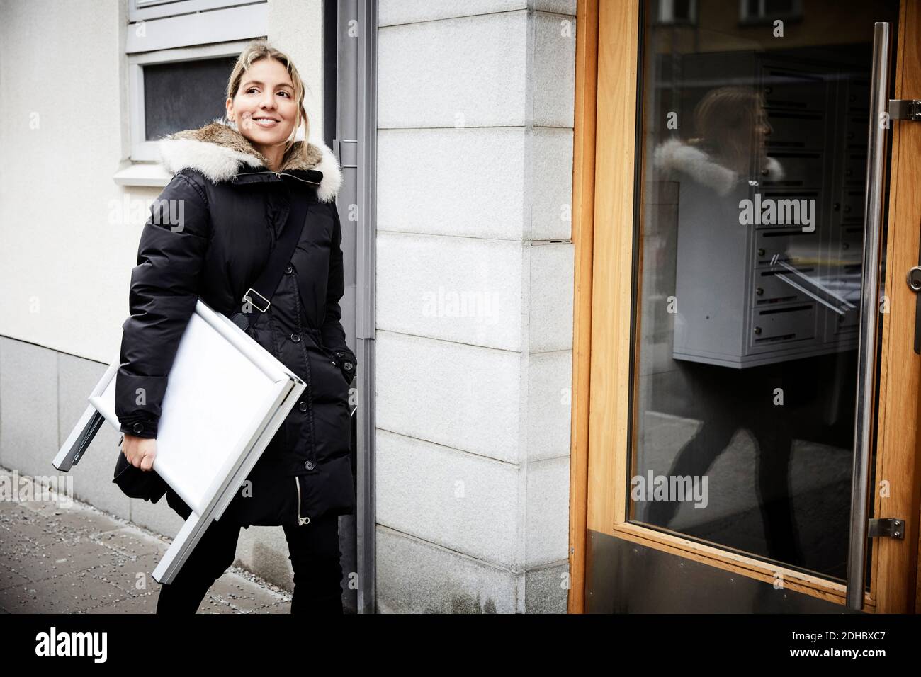 Selbstbewusste weibliche Immobilienmakler mit leerem Schild zu Fuß auf Bürgersteig in der Stadt Stockfoto