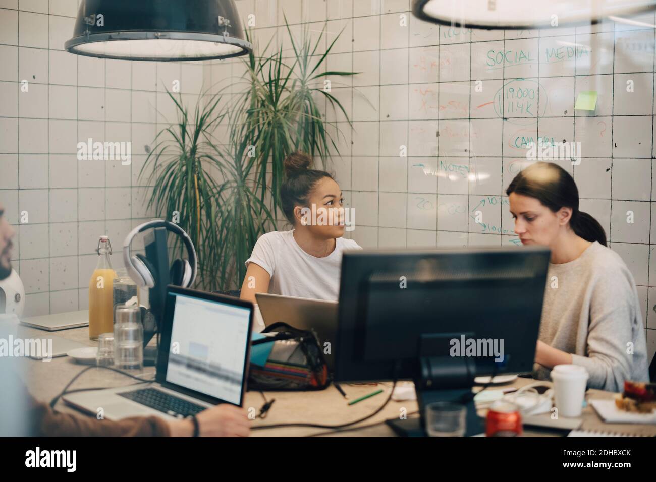 Multiethnische weibliche Hacker arbeiten am Schreibtisch im kreativen Büro gesehen Durchgangsfenster Stockfoto
