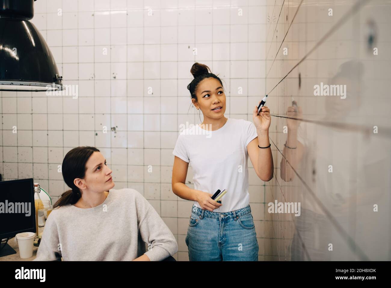 Junge Computerhacker erklären Strategie zu weiblichen Kollegen auf Fliesen Wand im Büro Stockfoto