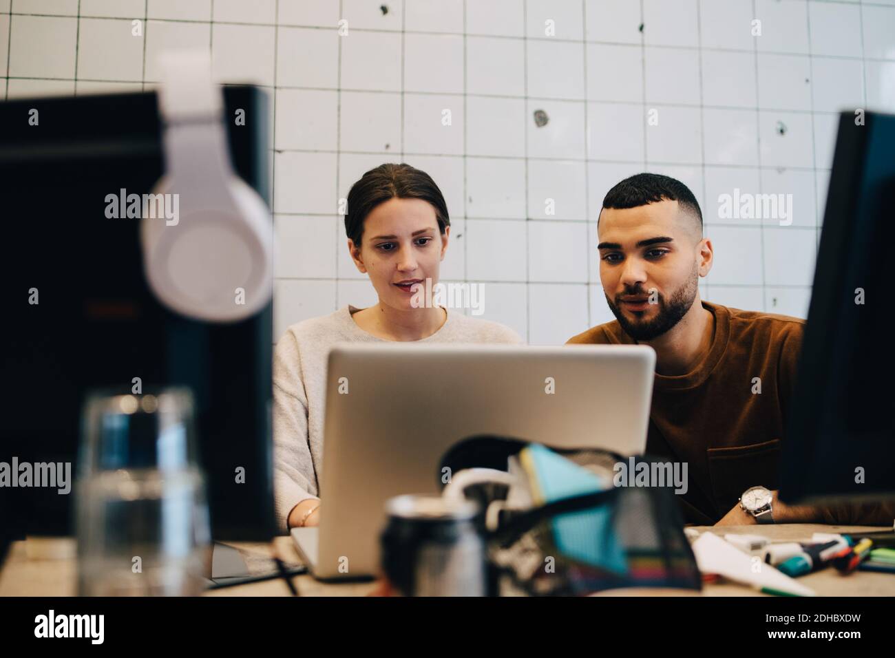 Selbstbewusste junge Kollegen und Kolleginnen mit Blick auf Laptop gegen Wand im Büro Stockfoto