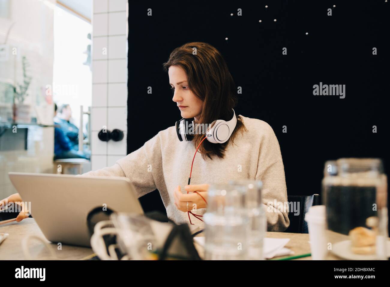 Junge weibliche Computerprogrammiererin mit Kopfhörern, die während des Sitzens arbeiten Schreibtisch in kleinen Büros Stockfoto