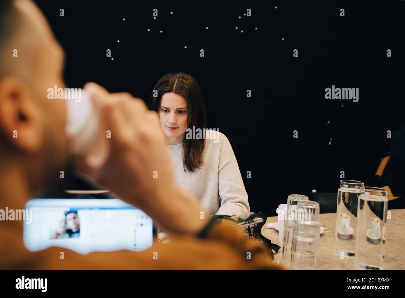 Männlicher Programmierer trinkt Kaffee, während zuversichtlich junge weibliche Hacker arbeiten Am Schreibtisch in einem kleinen Büro Stockfoto