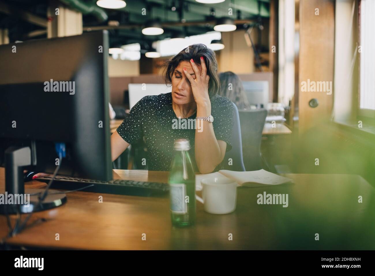 Müde Geschäftsfrau mit Kopf in der Hand sitzt am Computer-Schreibtisch Im Büro Stockfoto