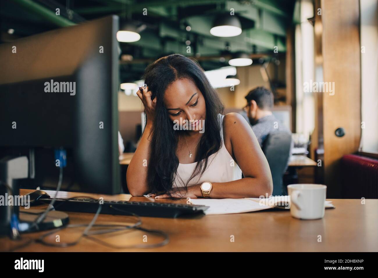 Geschäftsfrau mit Hand in den Haaren, die Buch an der Rezeption liest Büro Stockfoto