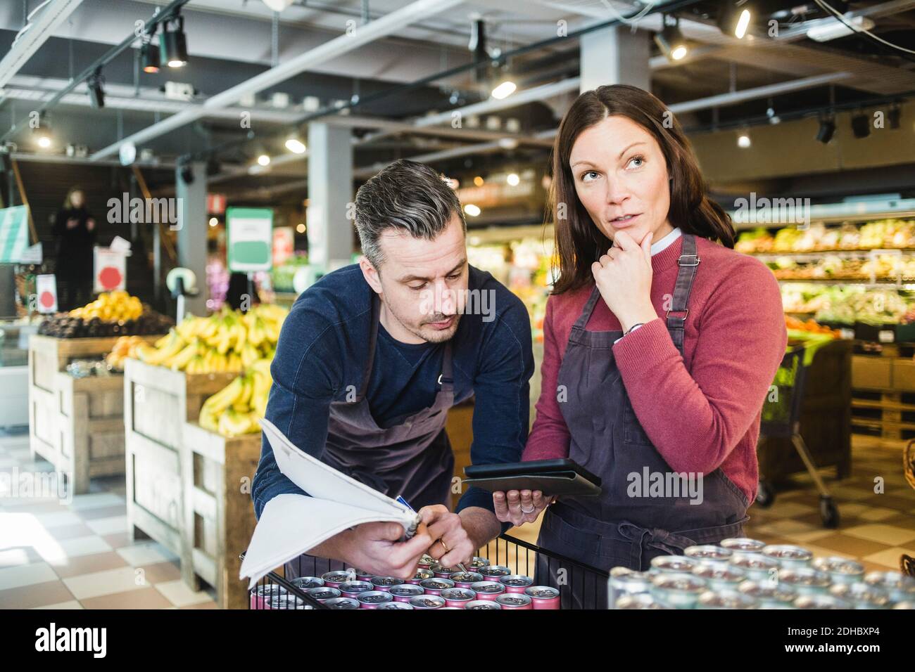Verkäufer mit Blick auf digitale Tablet von nachdenklichen Kollegen im Supermarkt Stockfoto