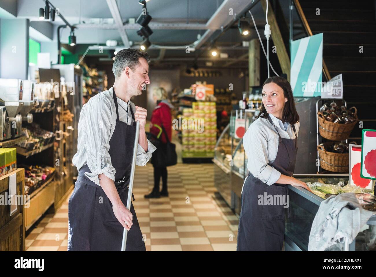 Lächelnder Verkäufer hält Besen, während er die Verkäuferin anschaut Supermarkt Stockfoto
