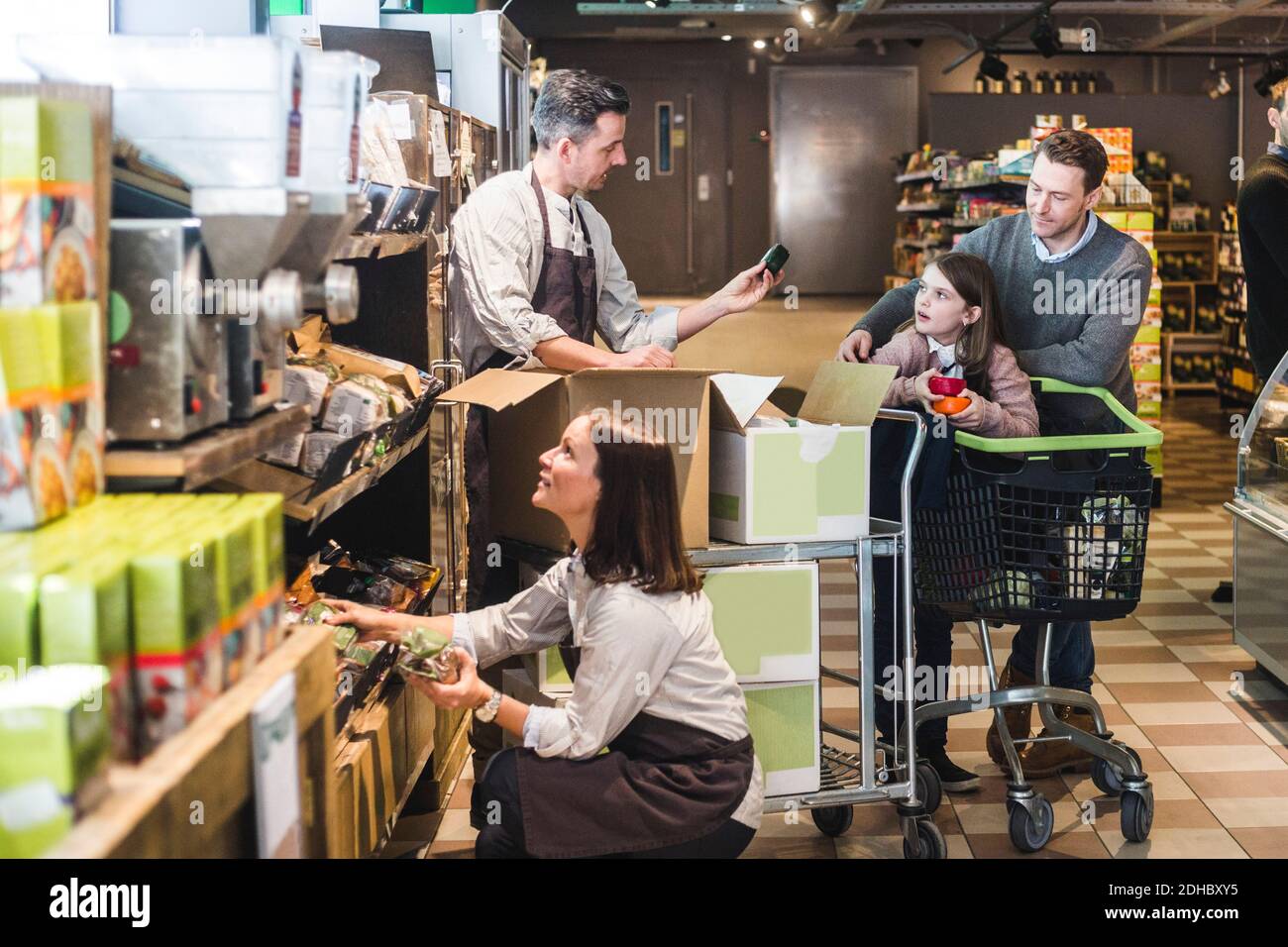 Verkäufer hilft Kunden, während Verkäuferin Regal im Supermarkt zu arrangieren Stockfoto